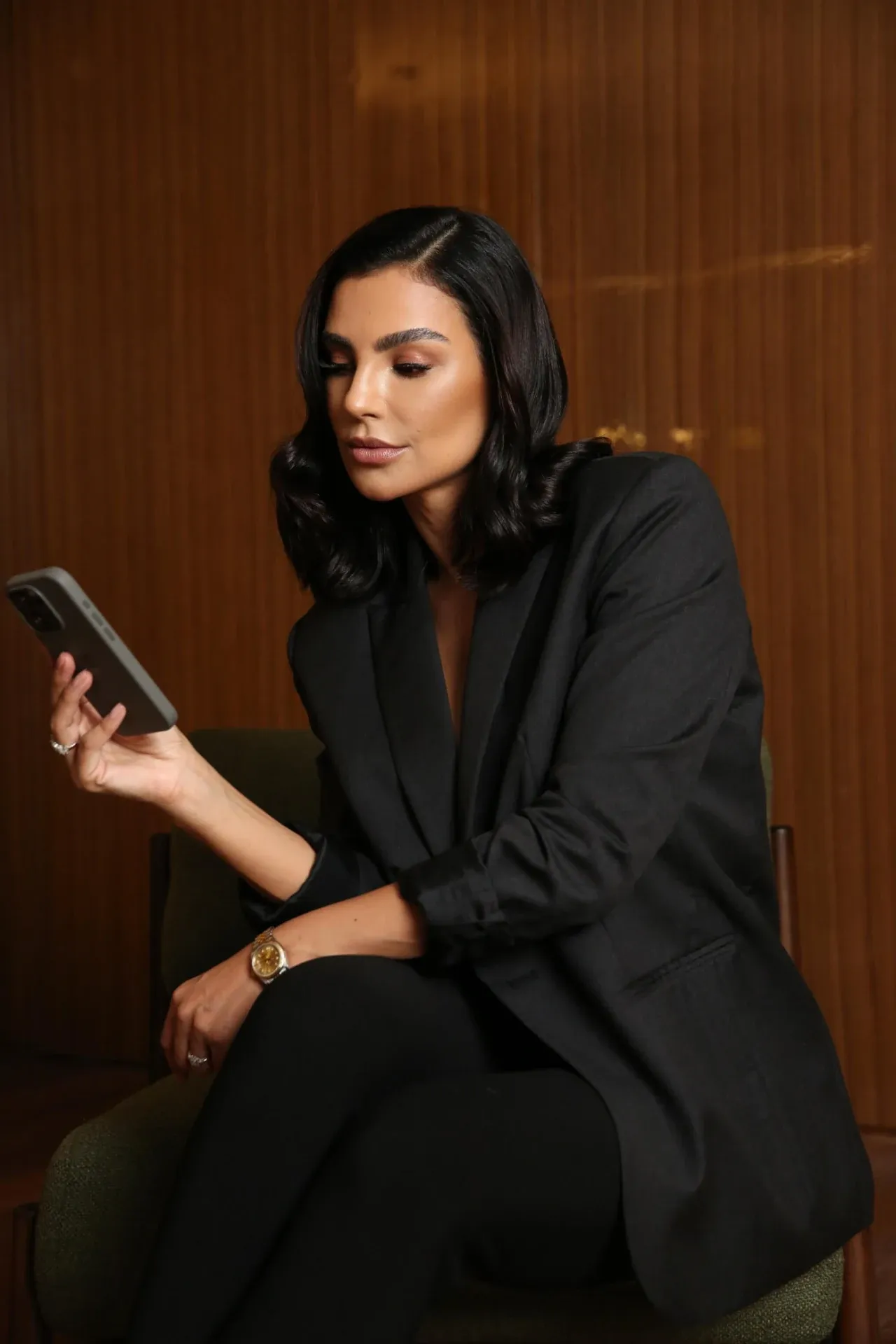 Cíntia Chagas sentada, de blazer preto, olhando para o celular